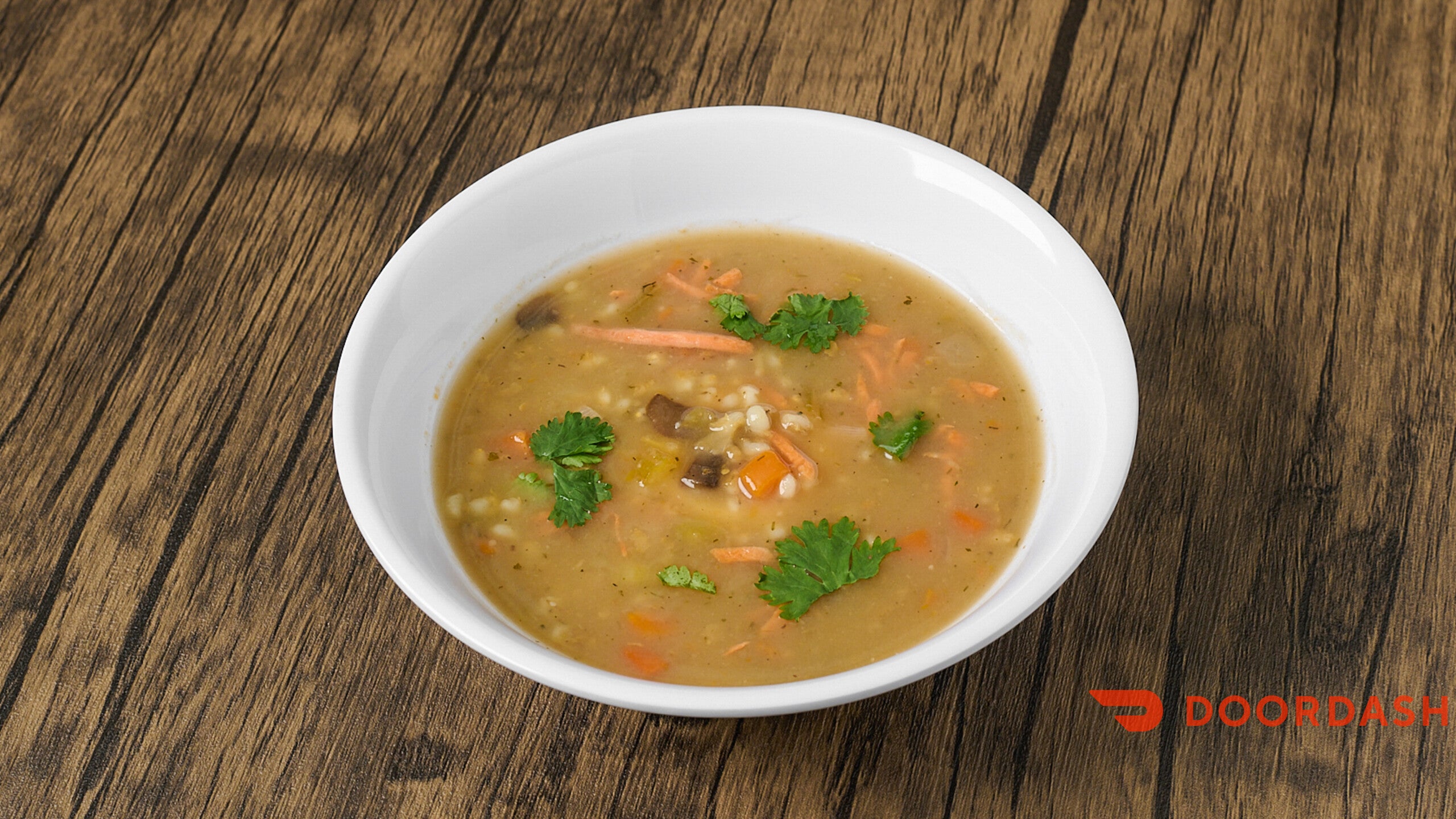 Bowl of soup with vegetables on a wooden table, featuring the Doordash logo.