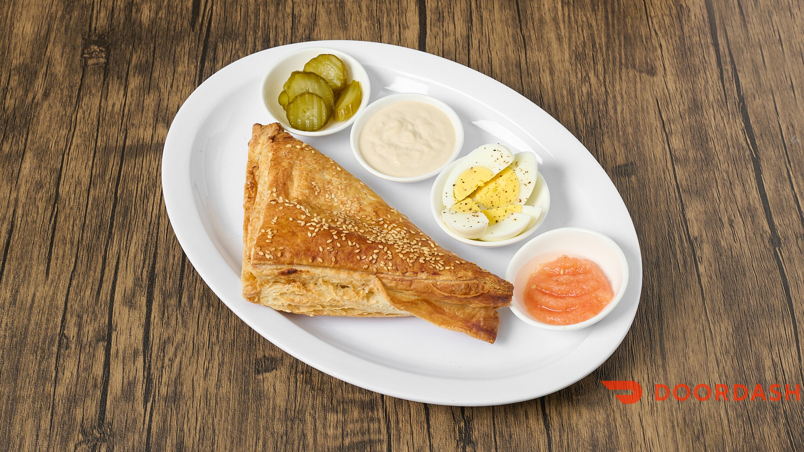 Platter with triangular bread, pickles, and dips on a wooden surface