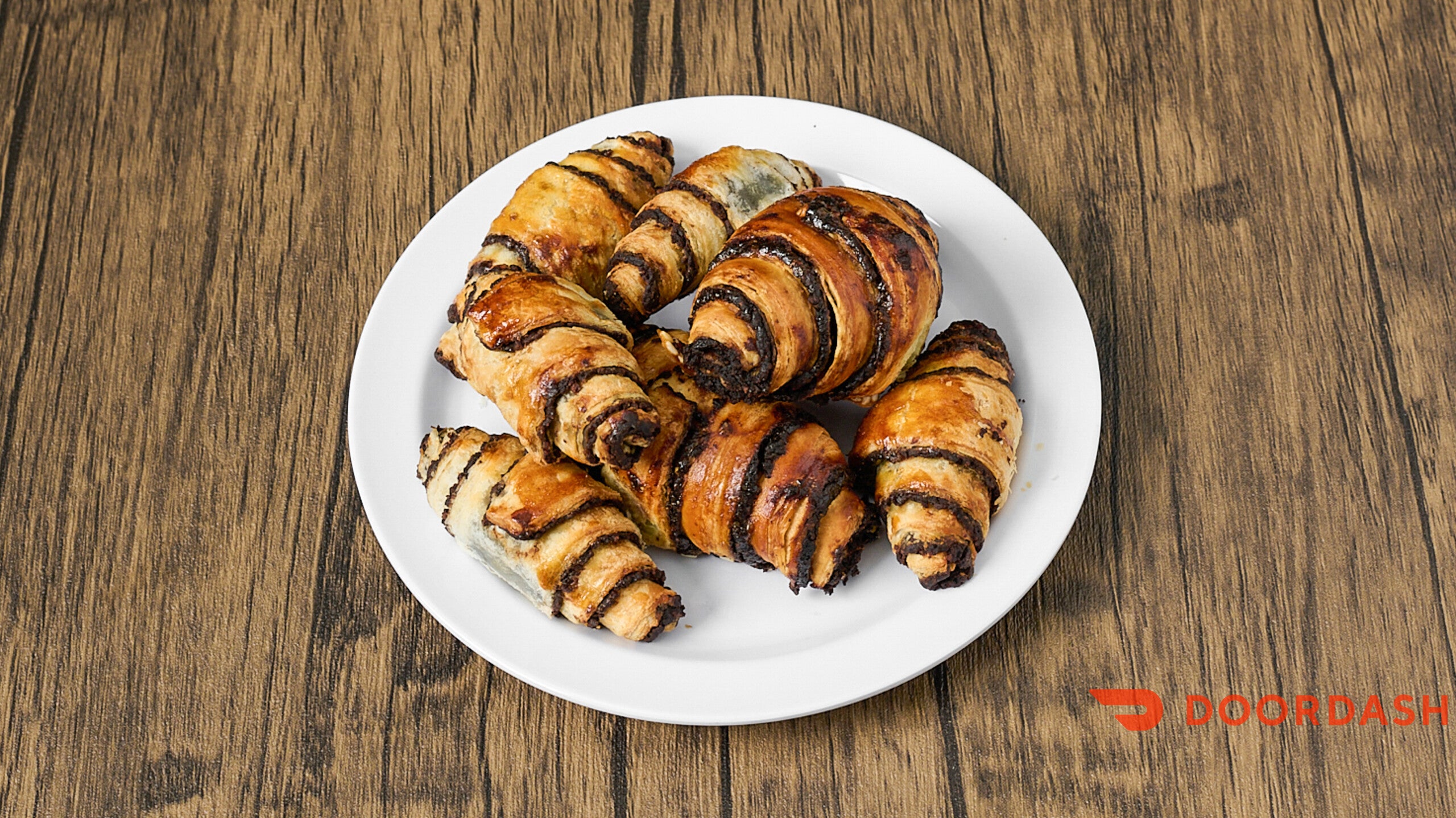 Rolls of pastry with chocolate filling on a white plate on a wooden surface, Doordash logo visible.