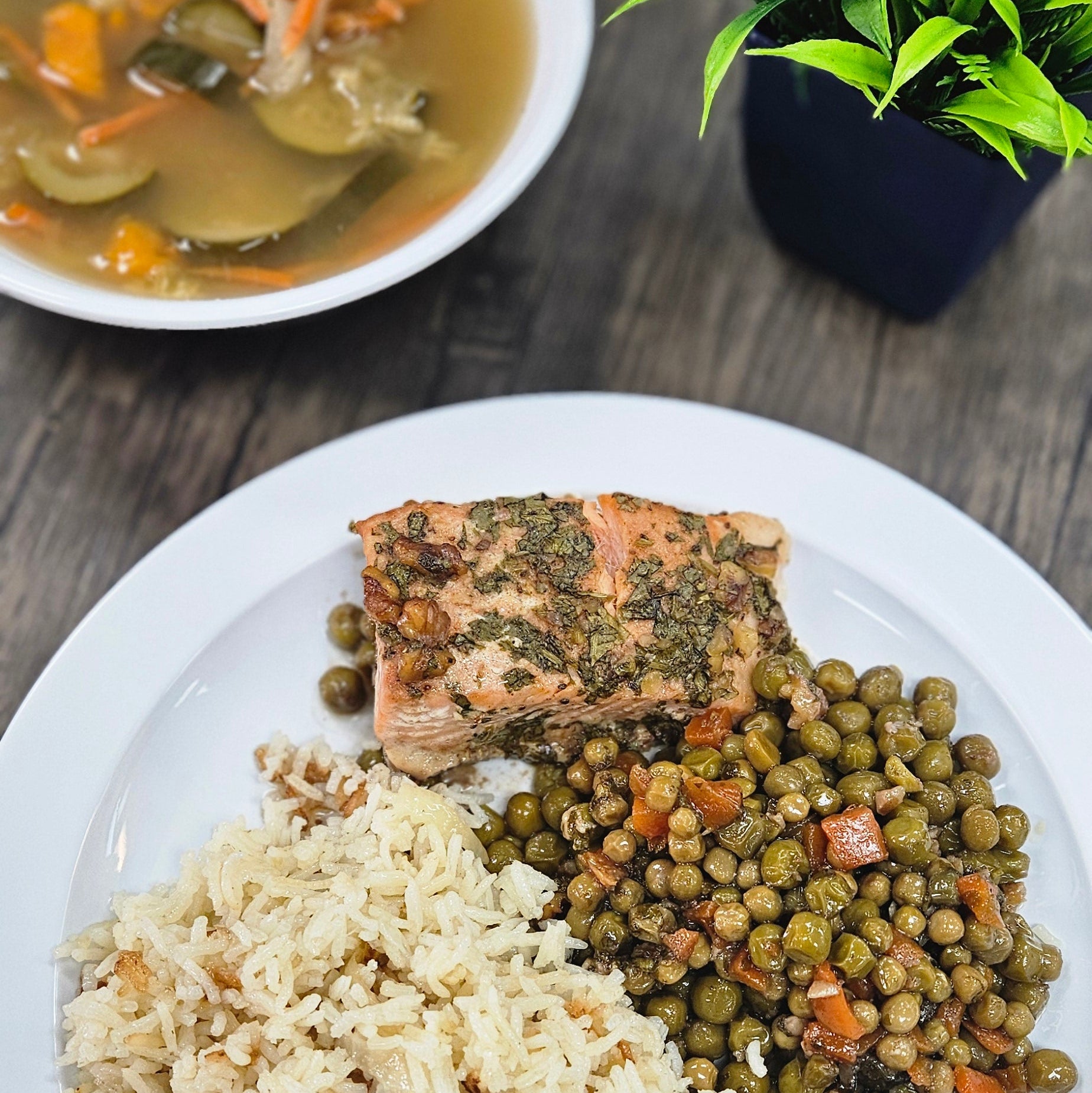 Plated meal with rice, beans, and fish on a wooden table with a plant.