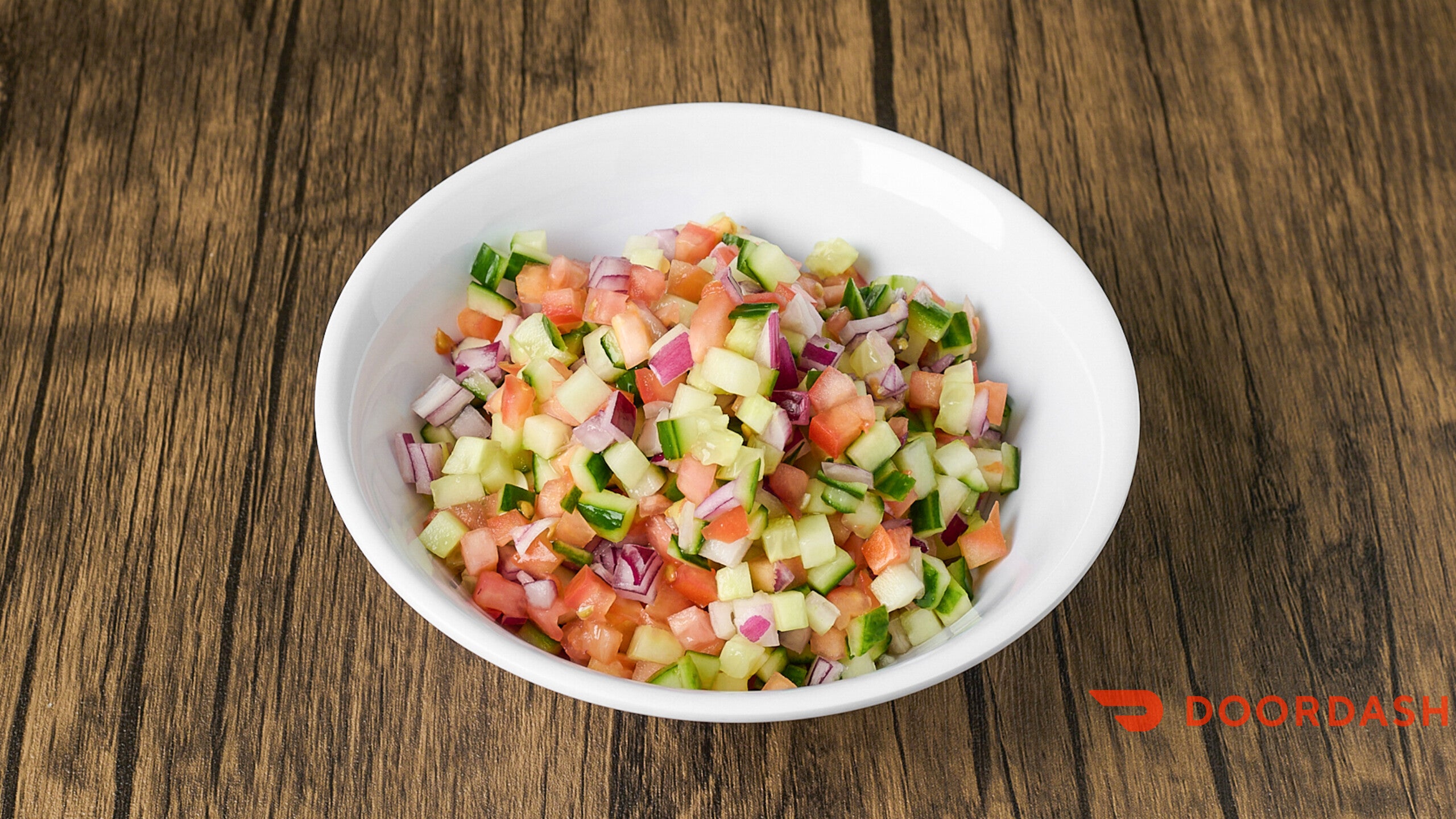 Colorful salad in a white bowl on a wooden surface with Doordash logo.