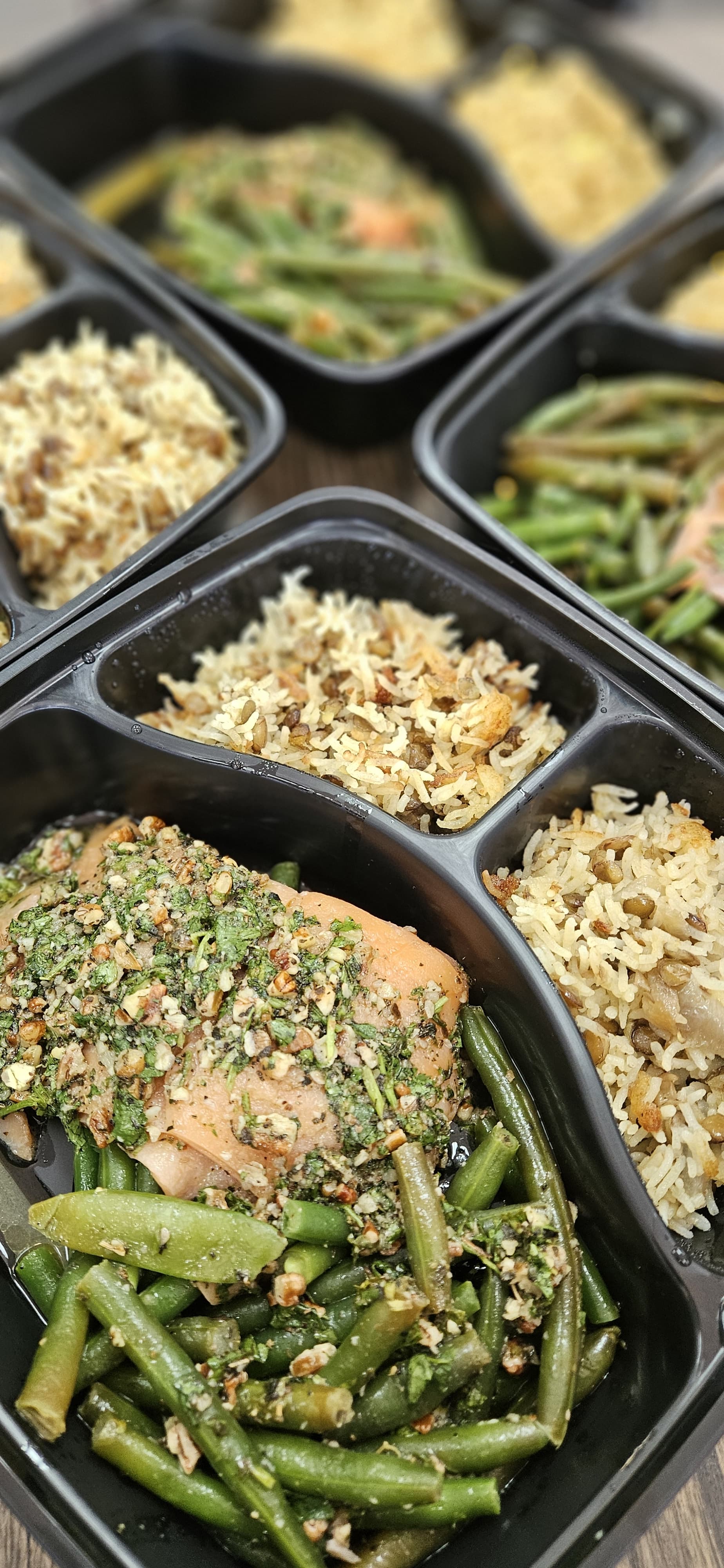 Prepared meals with chicken, green beans, and rice in black containers.
