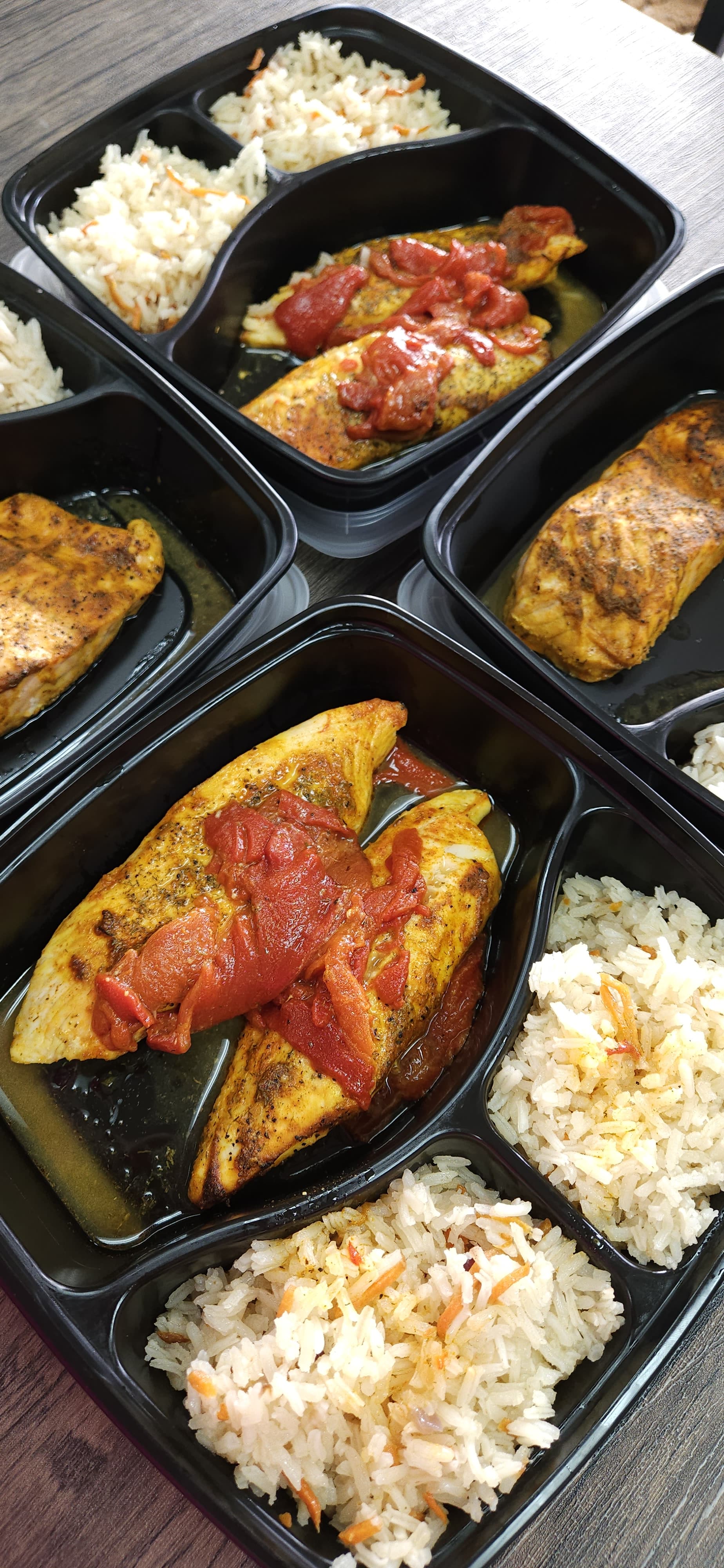 Prepared meals with chicken and rice in black containers on a wooden surface