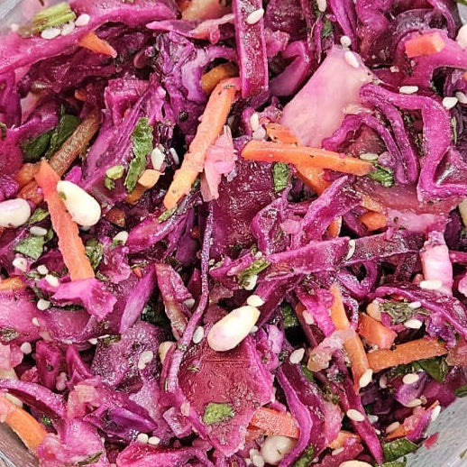 Purple cabbage salad with carrots in a clear plastic container on a dark surface
