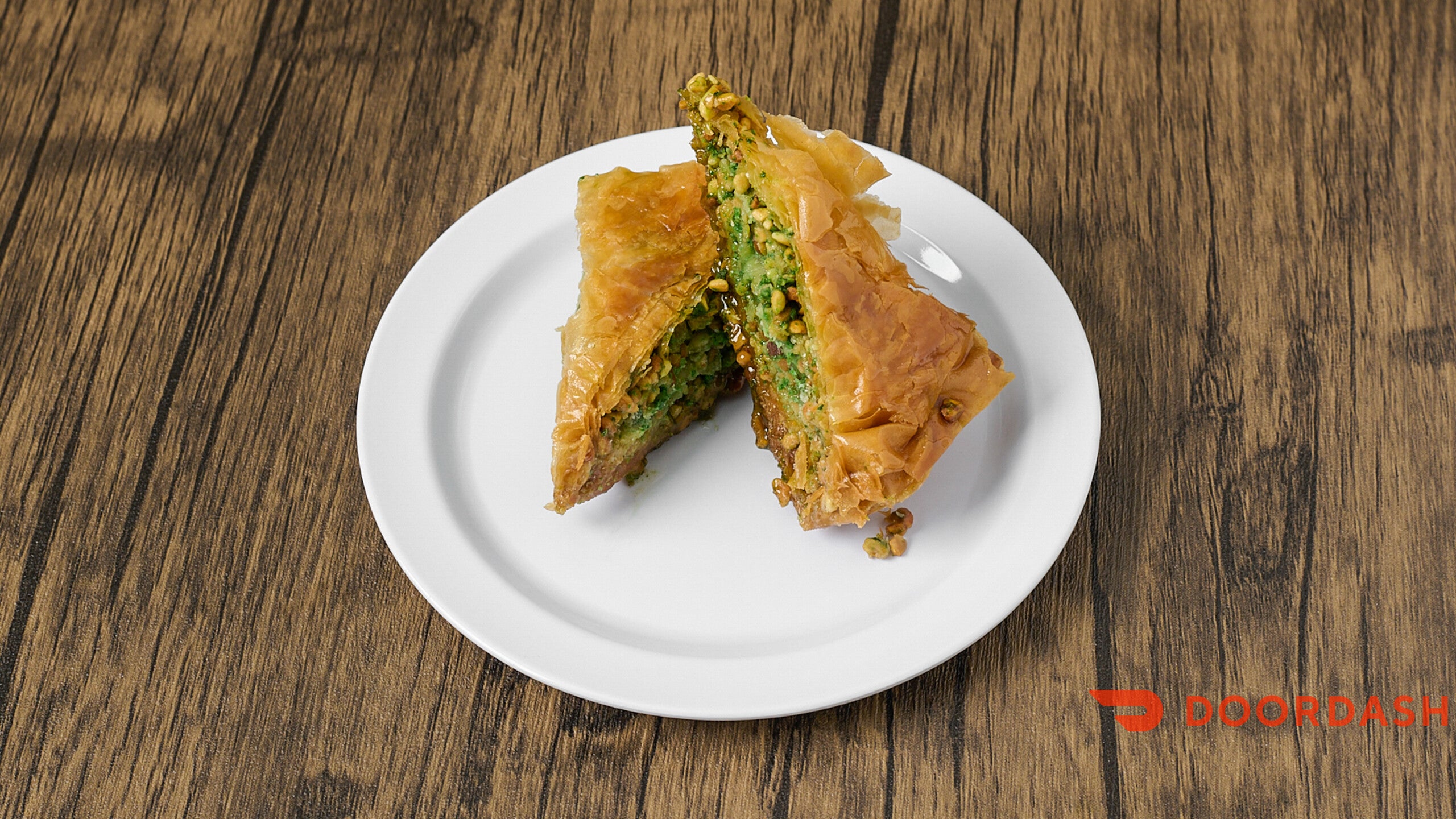 Two samosas on a white plate on a wooden table, with 'doordash' logo in the corner.