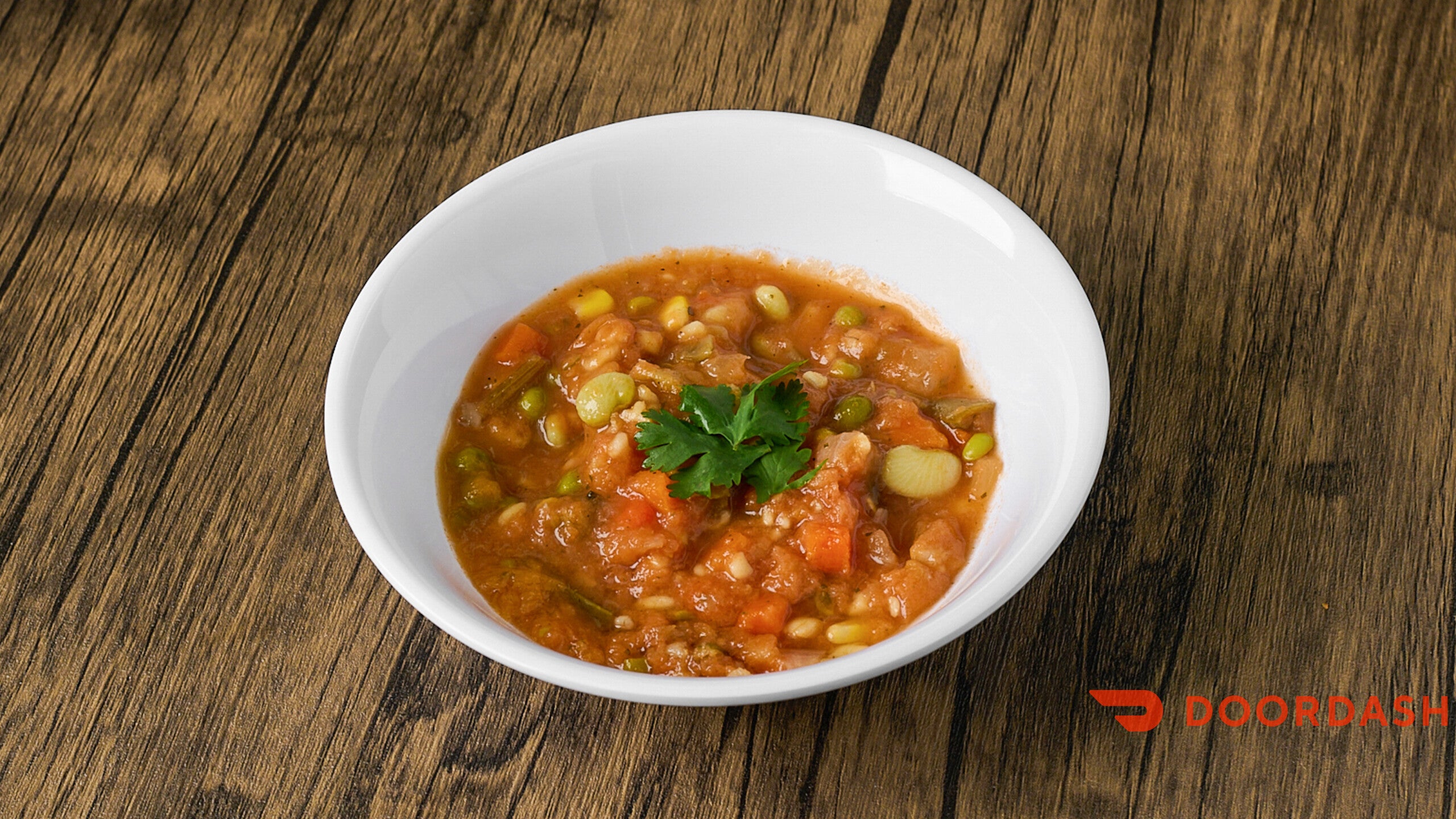 White bowl of soup with vegetables on a wooden table, featuring the DoorDash logo.