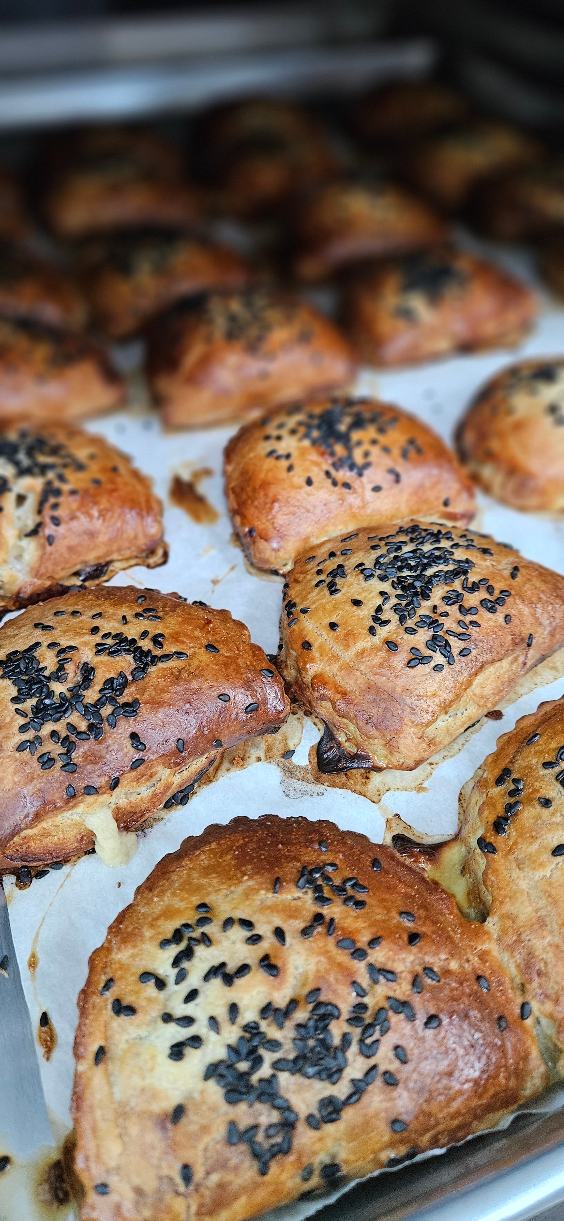 Baked burekas with sesame seeds on a baking tray